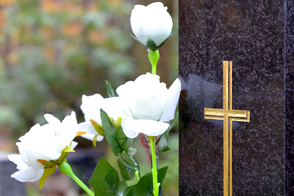 Gránit sírkő előtt fehér virágokból készült koszorú áll